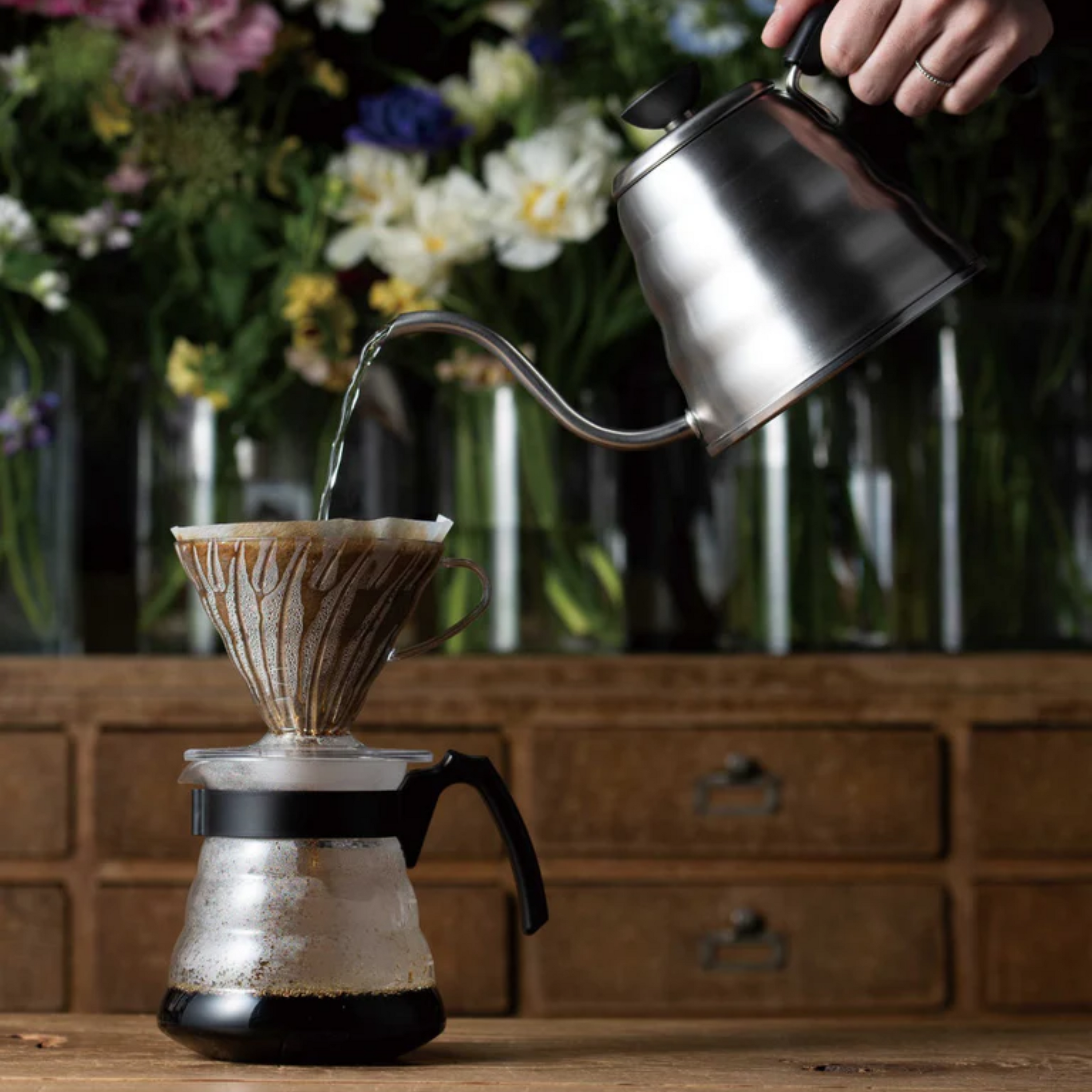Hand pouring hot water from a goose neck kettle into a pour-over