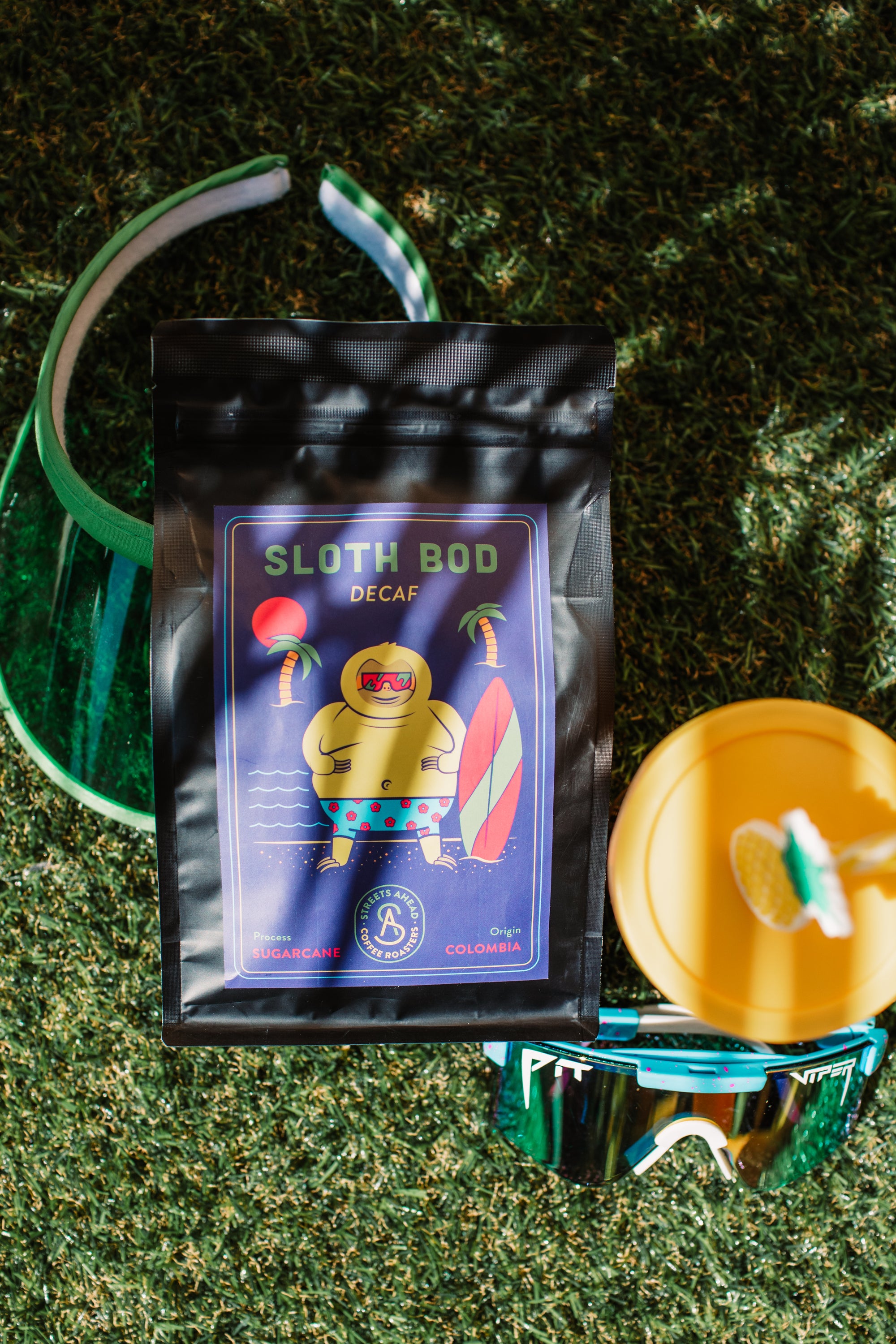 Sloth Bod coffee package with sunglasses and a drink on grass