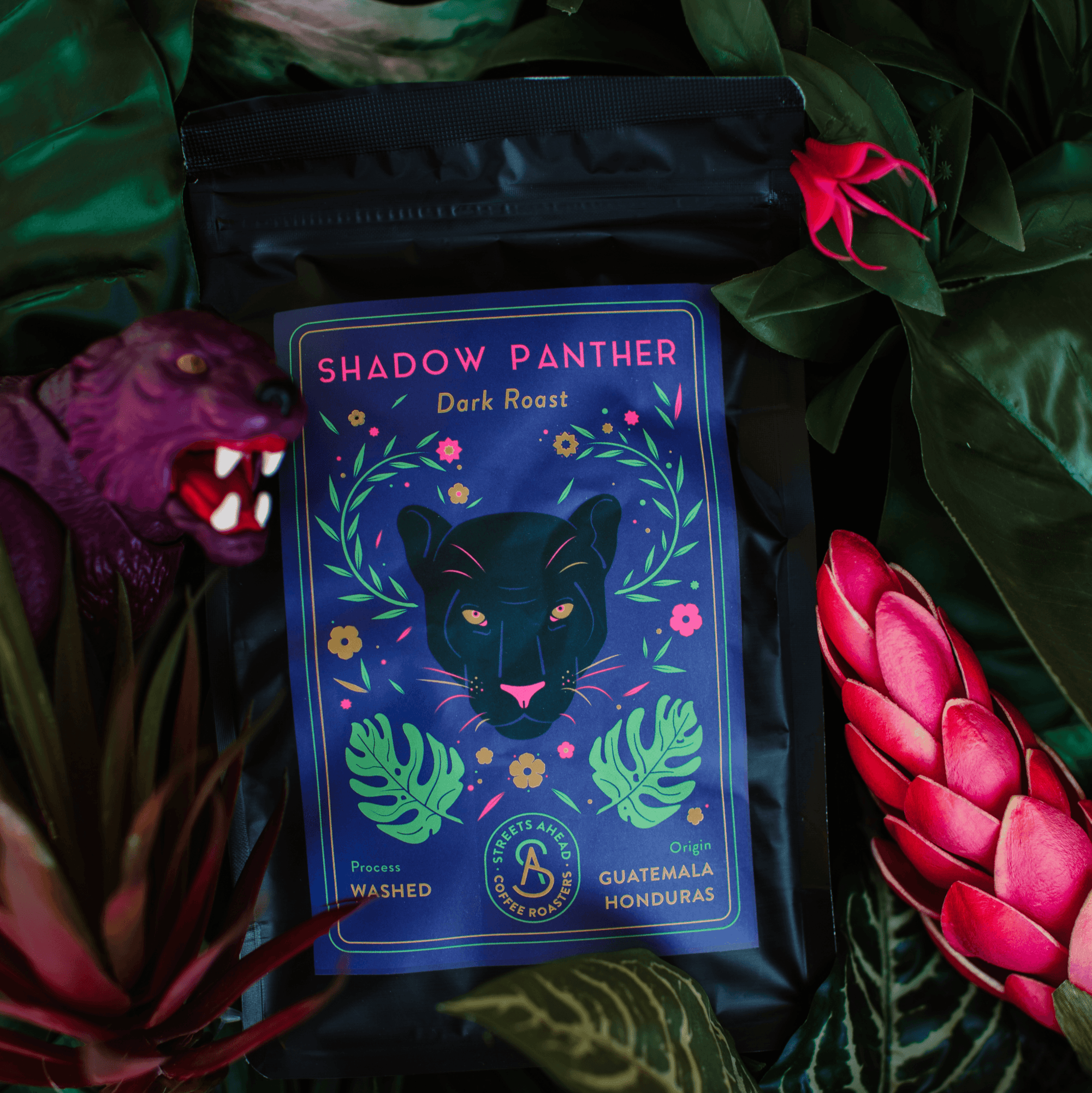 Dark roast, whole bean, specialty coffee bag featuring a drawing of a black panther, laying on top of green foliage and pink flowers.