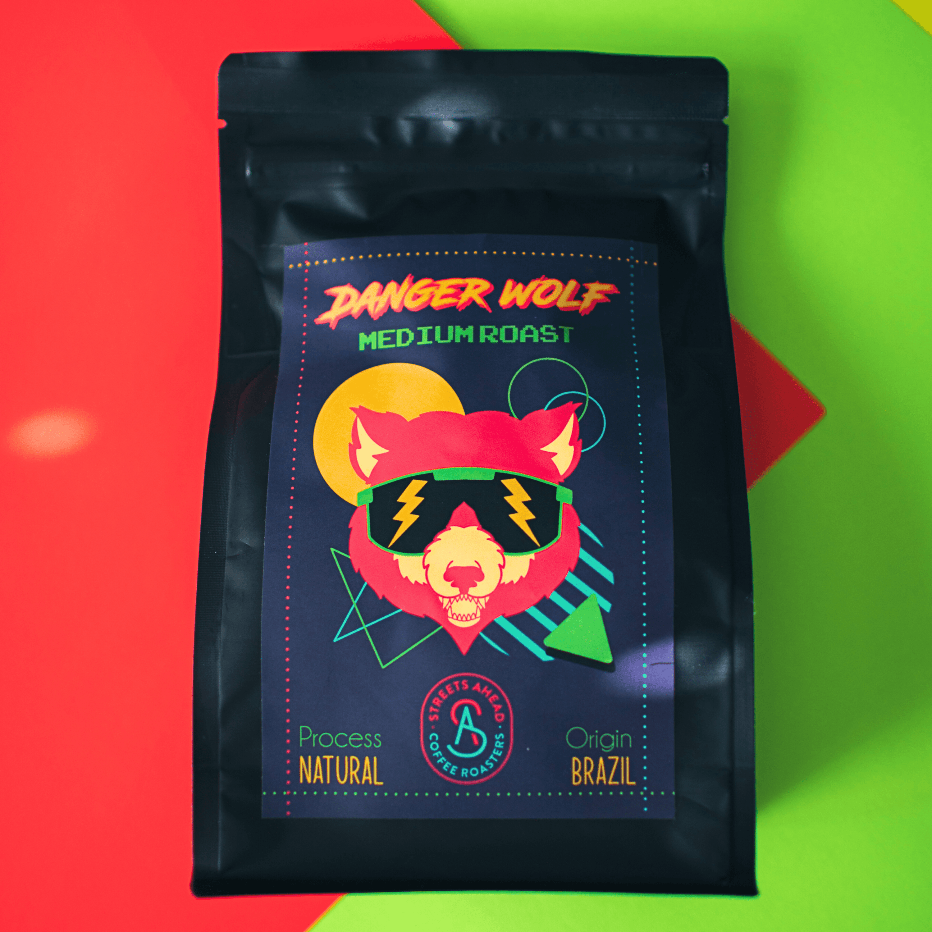 Medium roast, whole bean, specialty coffee bag featuring a drawing of a wolf with sunglasses, laying on top of neon paper.
