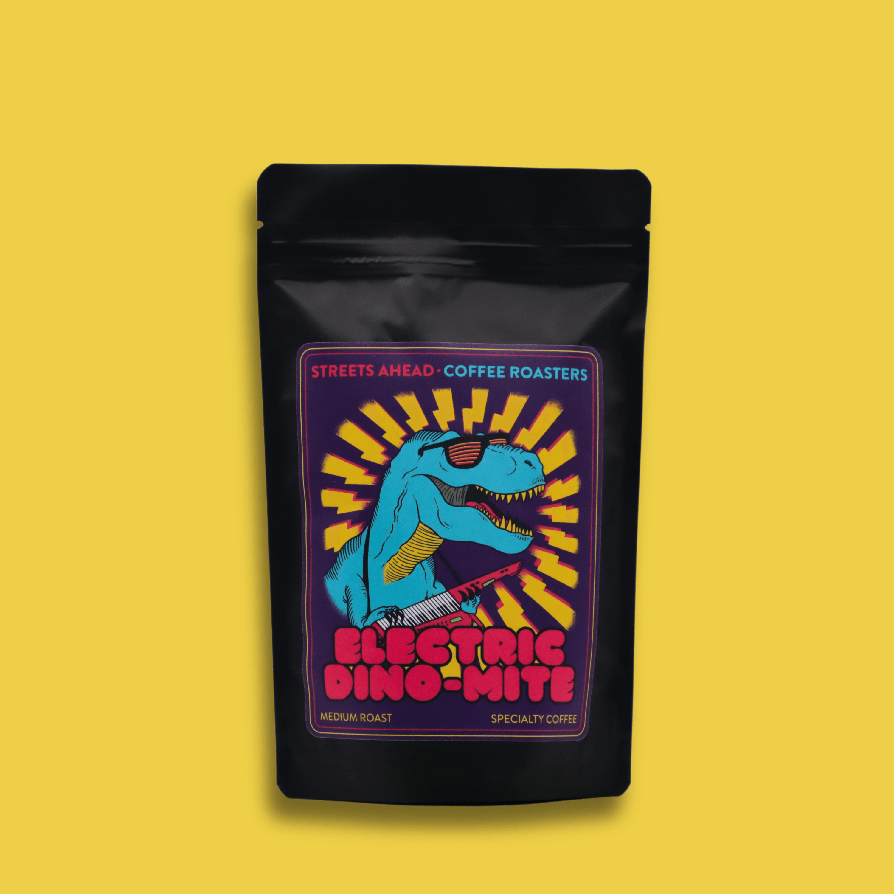 A 125g bag of medium roast, whole bean, Electric Dino-Mite specialty coffee in front of a yellow background.