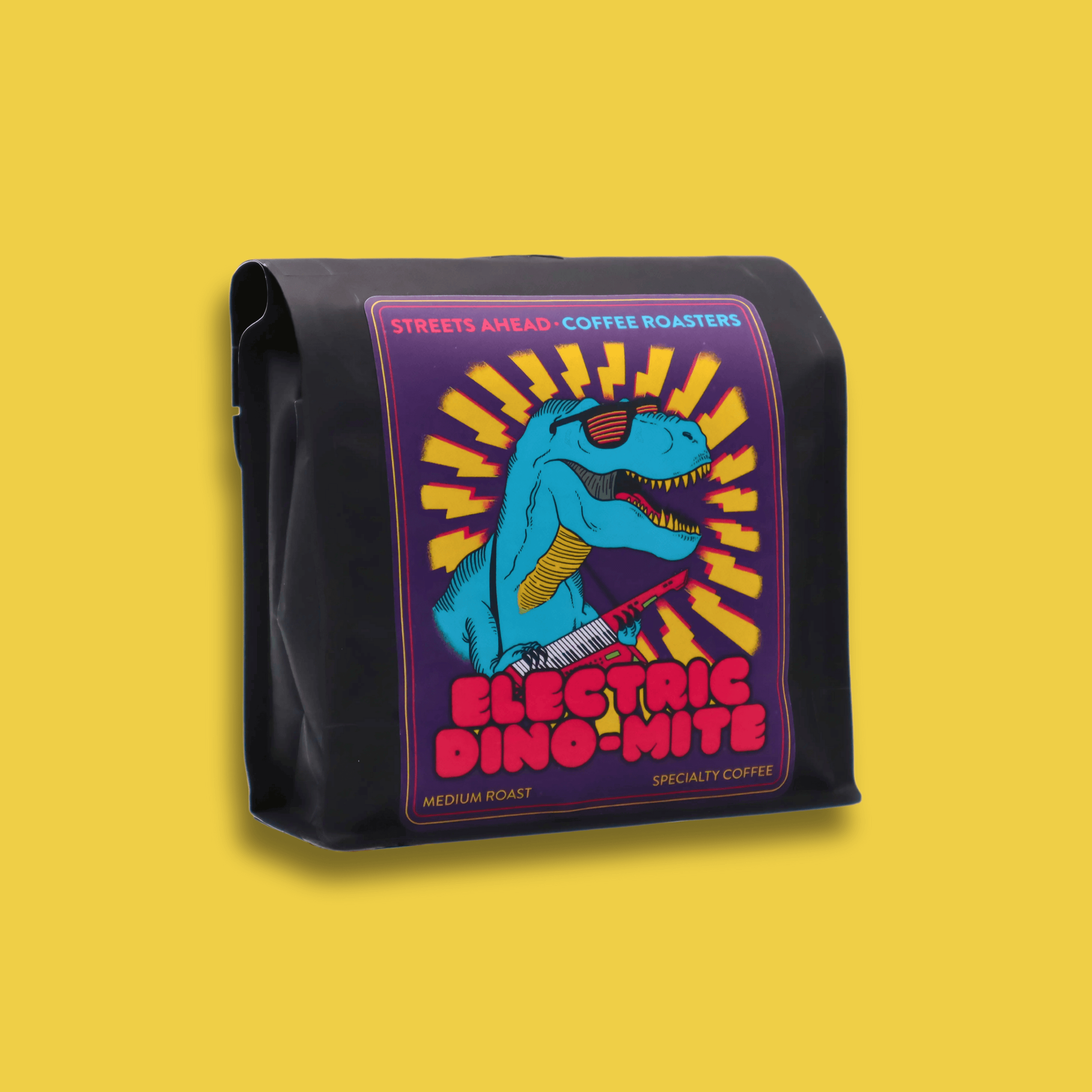 A 340g bag of medium roast, whole bean, Electric Dino-Mite specialty coffee sitting in front of a yellow background.